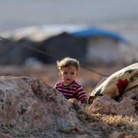 A newly displaced Syrian child walks near a refugee camp in Atimah village, Idlib province, on Tuesday. As Idlib offensive looms, thousands of Syrians flee to border villages