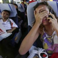 A Venezuelan migrant cries as she talks on the phone with her father, who is staying in Ecuador, as she boards a bus that will take her to the airport to fly back to her homeland, in Quito Wednesday. The woman will travel back home with a group of migrants in an airplane provided by the government of Venezuela. Diplomats meet over Venezuela migrant crisis as tens of thousands continue to flee