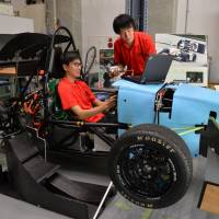 Hironori Nagata (right), leader of Formula Team FEM, stands beside a race car as Naoki Kosugi sits in the driver’s seat, at Nagoya University. The team is using crowdfunding to develop an electric car. As state subsidies decline, Nagoya University turns to crowdfunding to support student activities