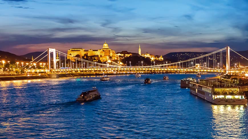 The grand Buda Castle and iconic Széchenyi Chain Bridge welcome travelers traversing the blue Danube in beautiful Budapest.