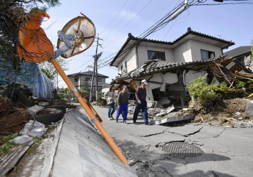 Residents survey damaged roads and toppled houses in the town of Mashiki, Kumamoto Prefecture, after a large earthquake in April 2016. | KYODO