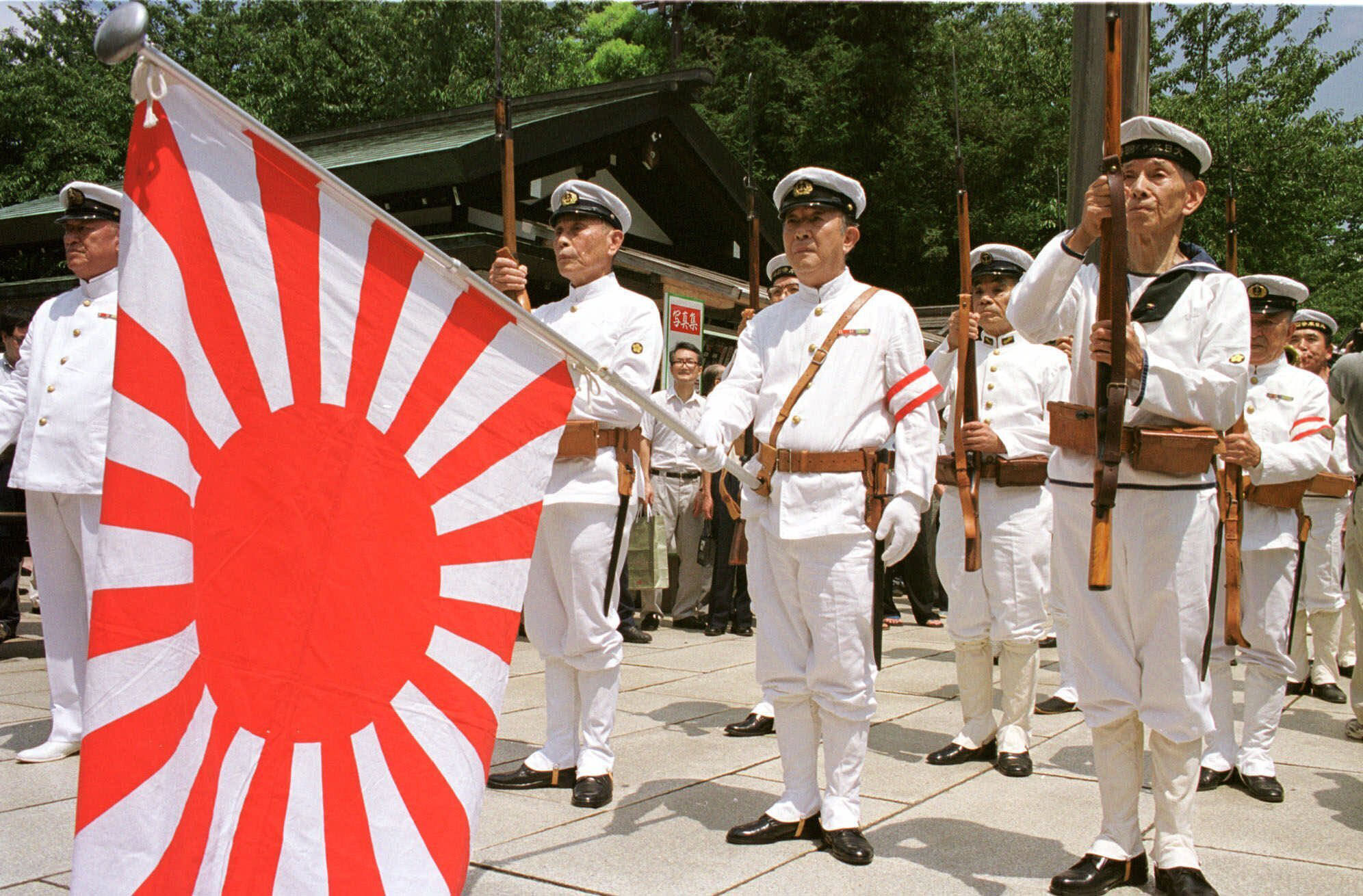 Japanese war veterans in the country's Imperial Navy uniform stand at attention with the navy flag as they pay their respects to the war dead at Tokyo's Yasukuni Shrine to commemorate the 54th anniversary of the end of World War II on Aug. 15, 1999. | AP