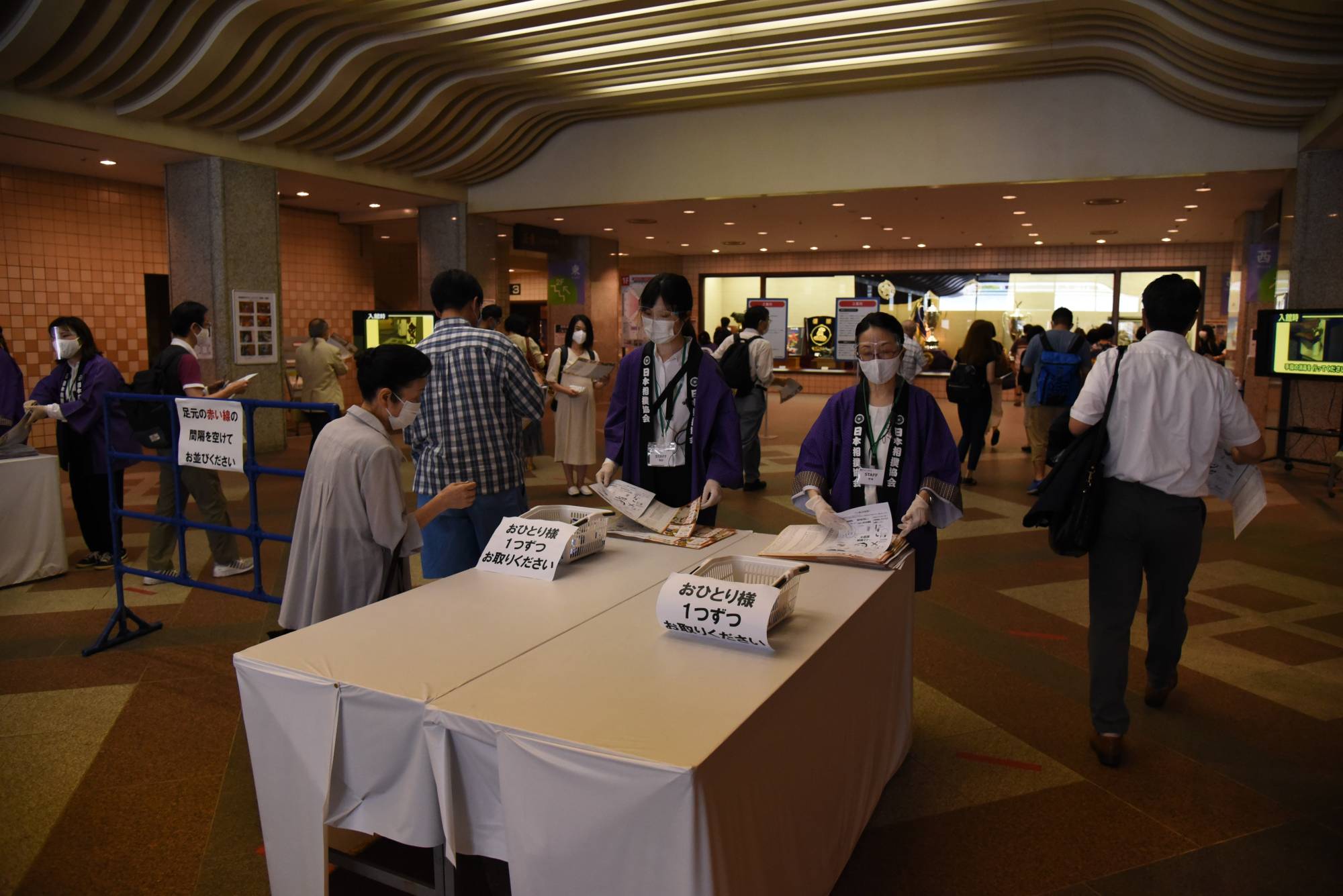 Staff wearing face shields hand out pamphlets to fans attending the Autumn Basho on Thursday at Ryogoku Kokugikan. | DAN ORLOWITZ 