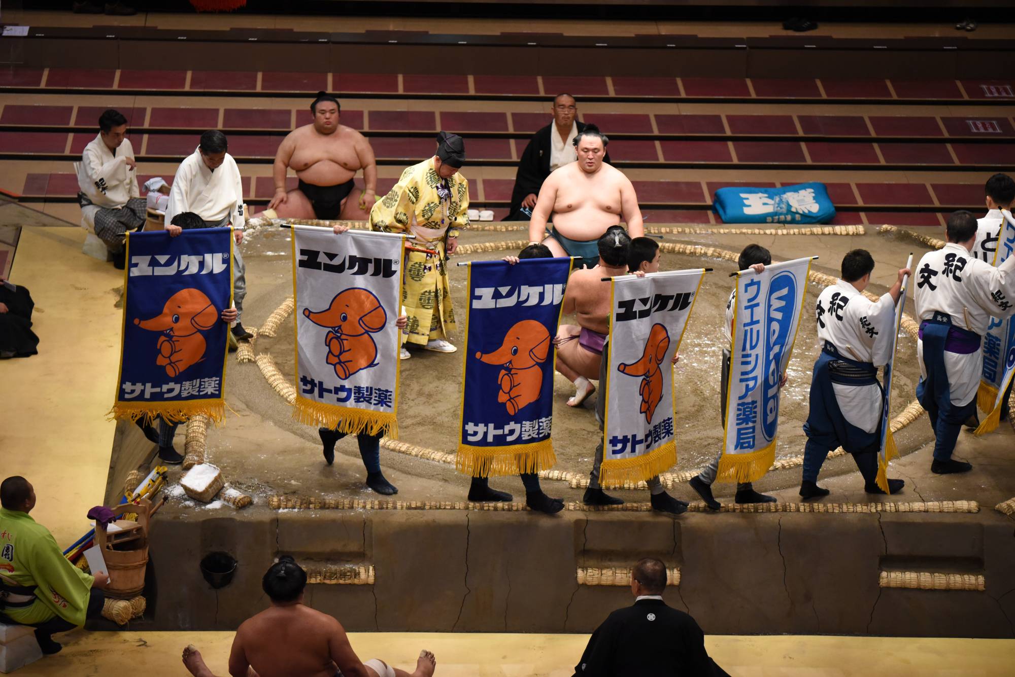 Attendants carry sponsor banners before a bout between Asanoyama and Tamawashi. | DAN ORLOWITZ 