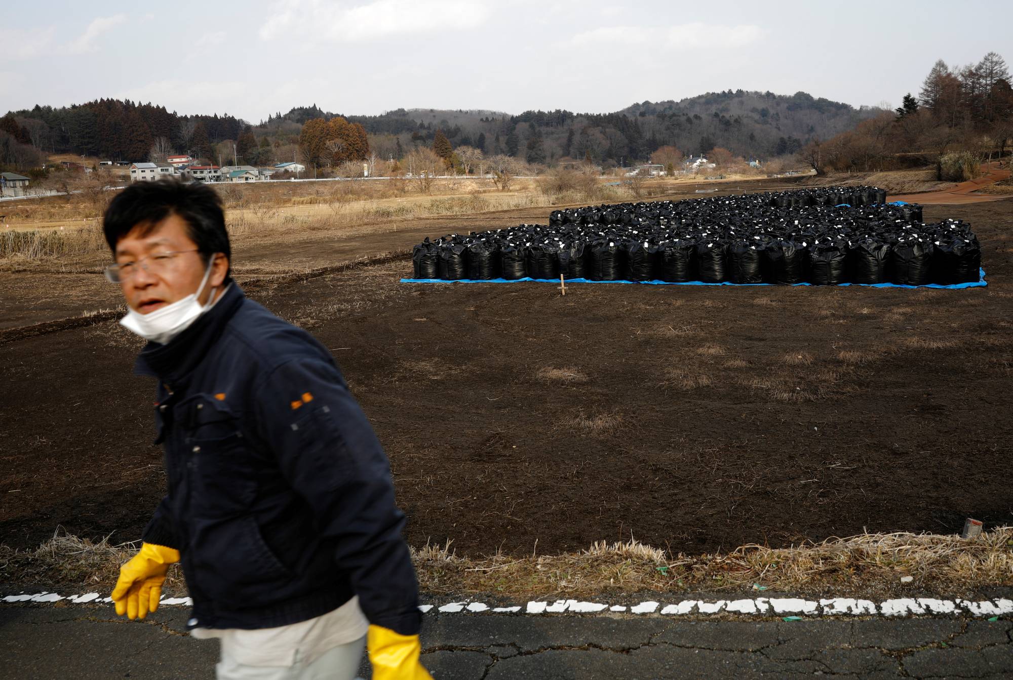 Sakae Kato walks past black bags containing contaminated soil from the fallout of the Fukushima nuclear plant, in a restricted zone in Namie, Fukushima Prefecture, on Feb. 21. | REUTERS