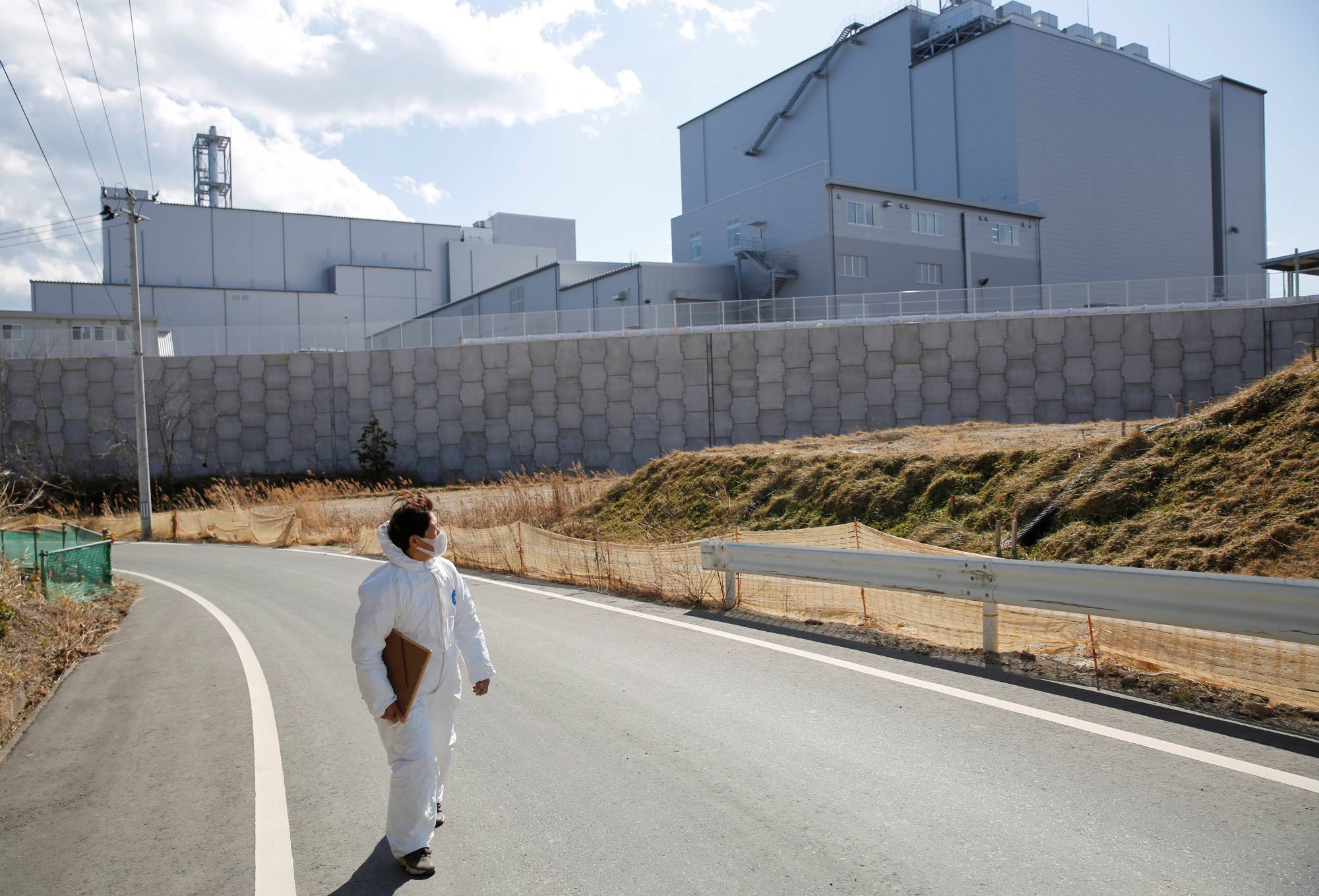 Hisae Unuma wears a protective suit as she walks past an incinerator which was built in a rural village near her collapsing home, where she lived before being evacuated. | REUTERS