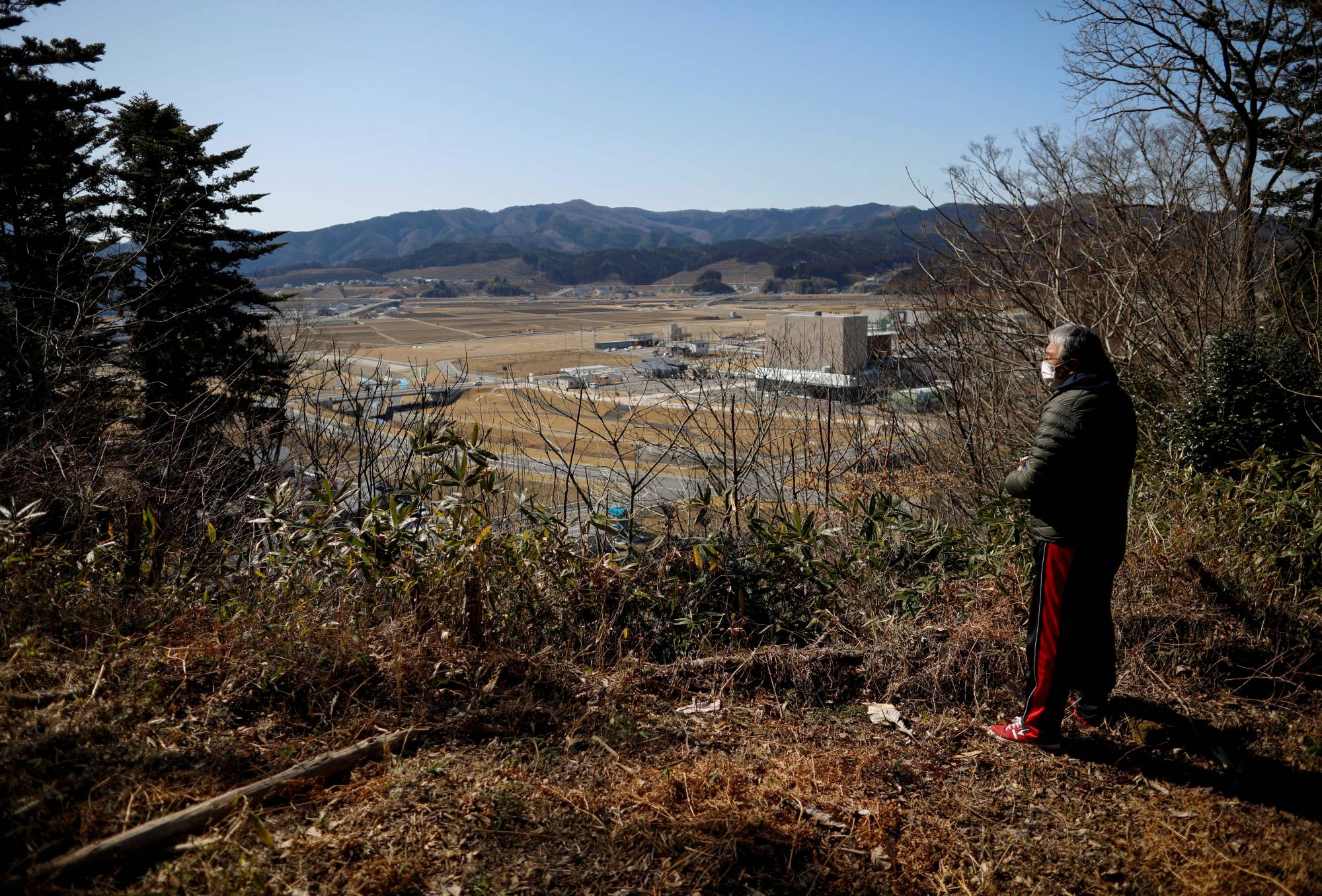 Kazuyoshi Sasaki looks at the former residential area which was devastated by the disaster, near the grave of his late wife ahead of the 10th anniversary the March 11 disaster, in Rikuzentakata, Iwate Prefecture | REUTERS