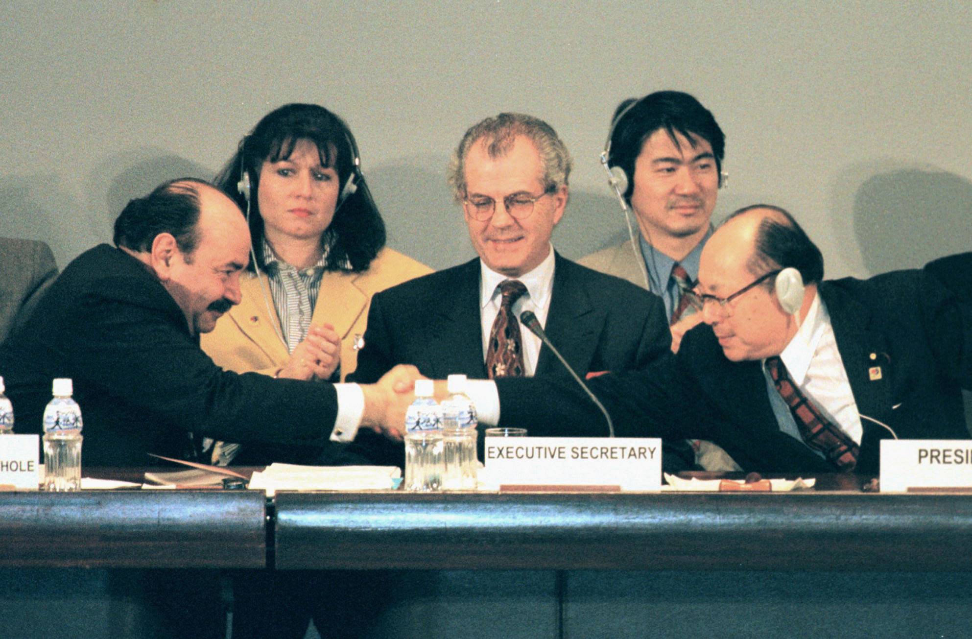 COP3 President Hiroshi Ohki shakes hands with Argentinian Ambassador Raul Estrada-Oyuela as Michael Zammit Cutajar, executive secretary of the U.N. climate process, looks on, after the closure of the meeting approving the Kyoto Protocol at the Kyoto International Conference Hall on Dec. 11, 1997. | KYODO