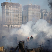 Firefighters work at the scene of a fire at Guryong village, the last slum in the glitzy Gangnam district, as apartment complexes which are currently under construction are seen in the background, in Seoul, on Friday. | REUTERS