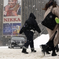 People walk in snow in Sapporo on Saturday. Heavy snow is likely to fall across much of Japan from Tuesday. | KYODO