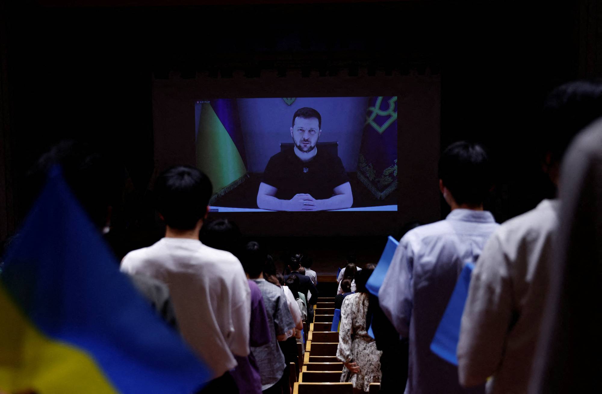 Attendants hold Ukrainian's national flags while Ukrainian President Volodymyr Zelenskyy gives an online speech at Toyo University in Tokyo last July. | REUTERS