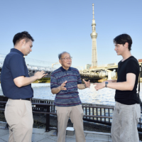 Tokyo Skytree serves as a backdrop as volunteer guide Toshio Takagi speaks with tourists in Tokyo’s Asakusa area. | ARC COMMUNICATIONS CO.
