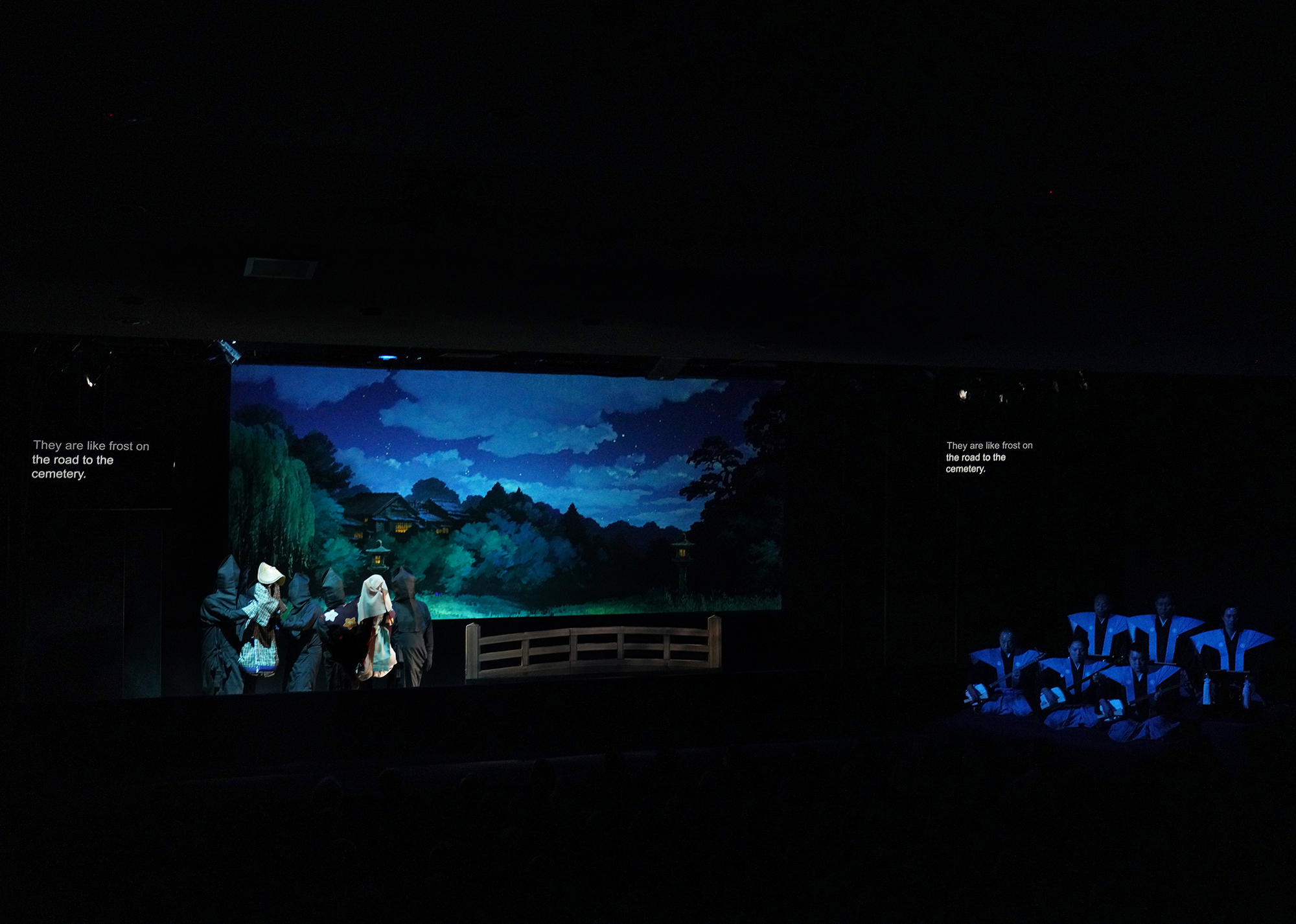 Bunraku puppets cross a stage with a newly added anime backdrop at a U.S. performance in October 2024, accompanied by musicians and narrators (right). | TOMOKO OGAWA